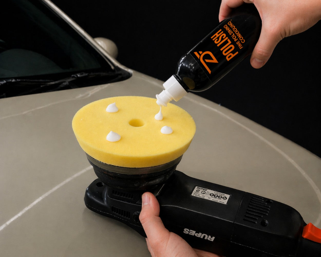 Person applying a product to a yellow polishing pad on a car surface