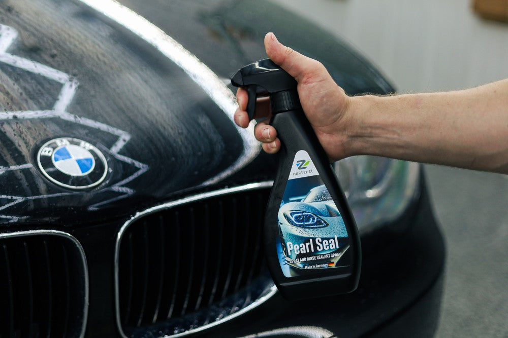 Person holding a bottle of Pearl Seal car care product in front of a BMW car